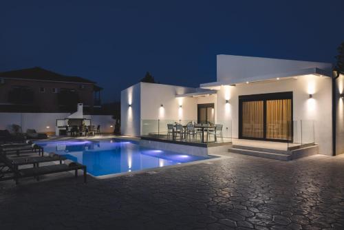 a swimming pool in front of a house at night at Villa De Reve in Laganas