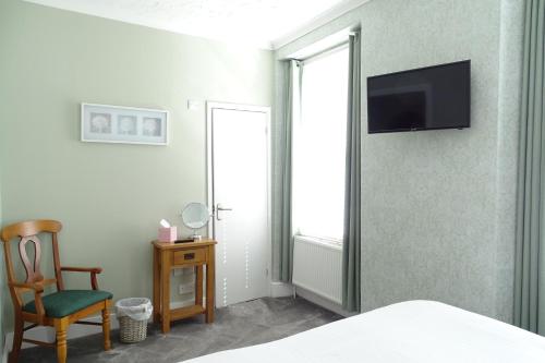 a bedroom with a chair and a television on a wall at The Melville in Brixham