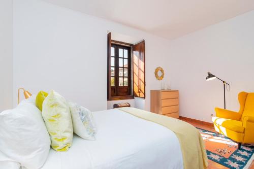a bedroom with a white bed and a yellow chair at Casa do Boco in Oliveira do Hospital