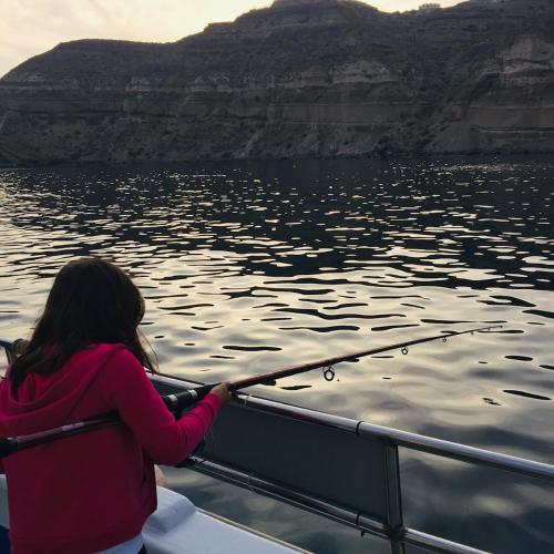 a young girl holding a pole on a boat in the water at Arcana Santorini Villas, An Authentic Cycladic Experience in Akrotiri