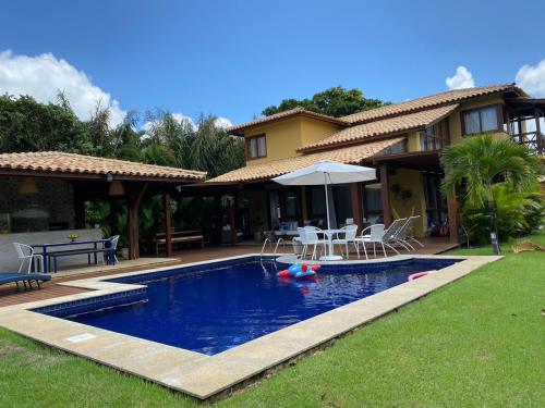a house with a pool with chairs and an umbrella at Costa do Sauipe Casa dentro do complexo hoteleiro in Costa do Sauipe