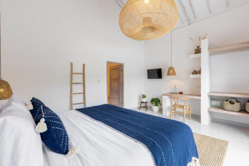 a white bedroom with a blue and white bed and a desk at Jepun Sari Uluwatu in Uluwatu