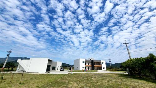 a cloudy sky above a white building and a field at Clare Holiday B&B in Checheng