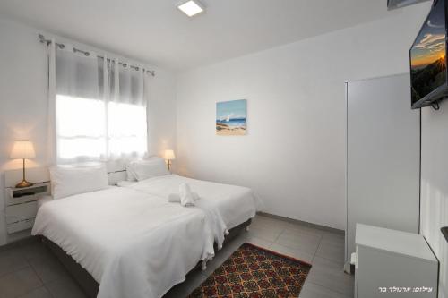 a white bedroom with two beds and a window at וילה מגדלא in Migdal