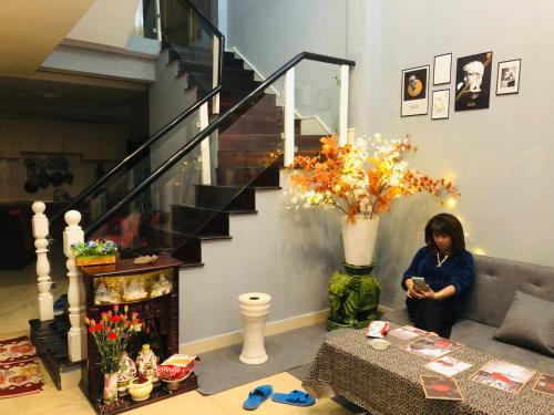 a woman sitting in a living room with a vase of flowers at SINH ĐÔI HOUSE in Da Lat