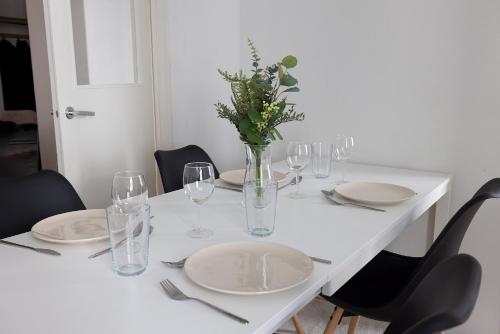 Biały stół z talerzami i kieliszkami oraz waza z kwiatami w obiekcie 2ndhomes Cozy and Quiet 2BR Apartment by the Esplanade Park w Helsinkach