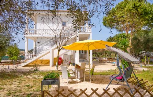 a yellow umbrella sitting in the sand in front of a house at Katoi Studios Agios Georgios Pagoi in Agios Georgios Pagon