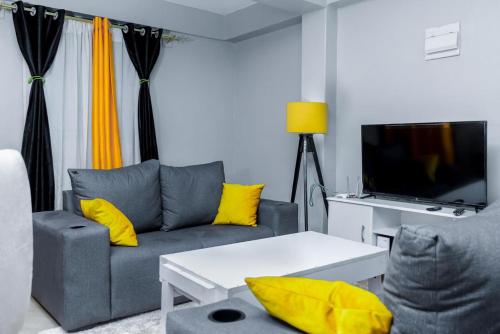a living room with a gray couch and yellow pillows at Stay.Plus Oark Apartment Kisii in Kisii