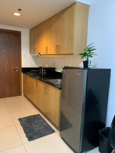 a kitchen with a black refrigerator and wooden cabinets at Cozy Crib - Shell Residences Condominium in Manila
