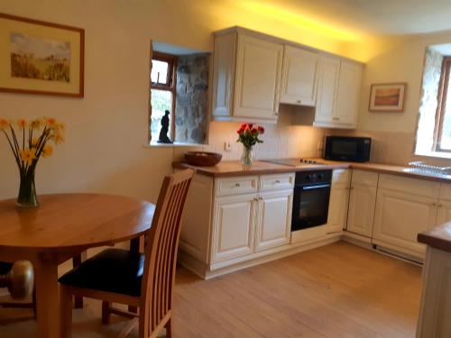 a kitchen with white cabinets and a wooden table at Plough Cottage is a 18th Century barn conversion offering a tranquil rural retreat 9 miles from the Lake District National Park in Carnforth