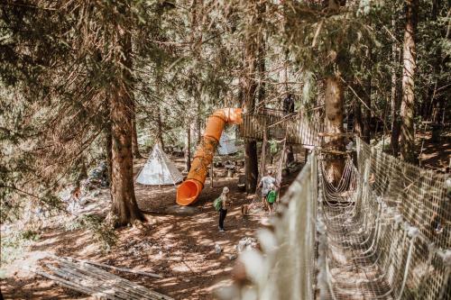 a group of people walking through a forest with an orange slide at Familienhotel Huber in Valles