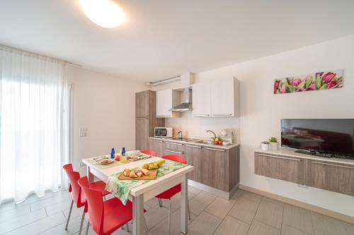 cocina y comedor con mesa y sillas rojas en Residenza Monica, en Lignano Sabbiadoro