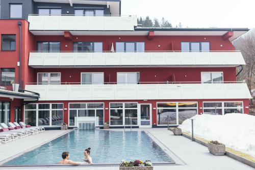 two people in a swimming pool in front of a building at Das Kaiserblick 4 Sterne Superior in Ellmau