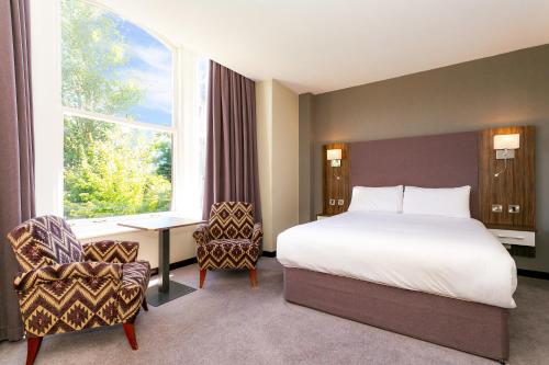 a bedroom with a bed and a desk and a window at Cedar Court Hotel Harrogate in Harrogate