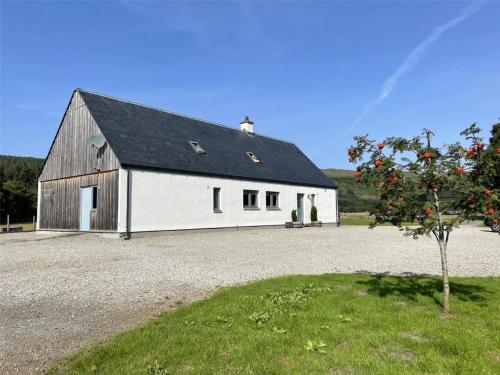 a white barn with a black roof and a tree at Highland Hideaway in secluded riverside location in Garve