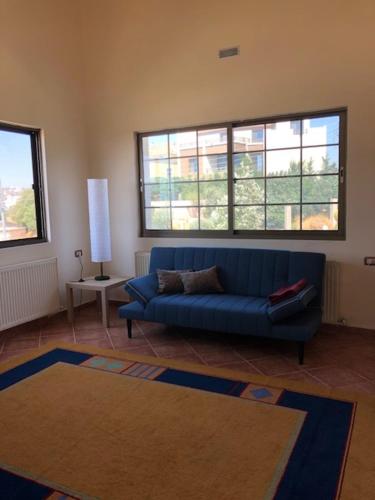 a living room with a blue couch and two windows at Charming House in Amman + Balcony in Amman