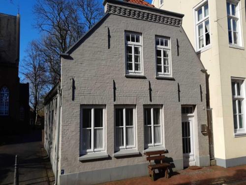 ein graues Haus mit weißen Fenstern und einer Bank davor in der Unterkunft Ferienwohnung am Kirchplatz 25561 in Weener