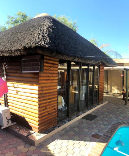 a small hut with a thatched roof next to a pool at Oppi Draai Guesthouse in Oudtshoorn