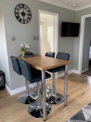 a dining room table with chairs and a clock on the wall at Modern 2 Bed Chalet - 27 Bermuda Holiday Park in Hemsby