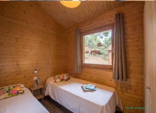 two beds in a wooden room with a window at Camping Cala Llevado in Tossa de Mar