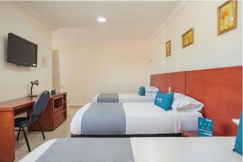 Habitación de hotel con 2 camas, escritorio y TV. en Hotel Rivera Del Mar en Barranquilla