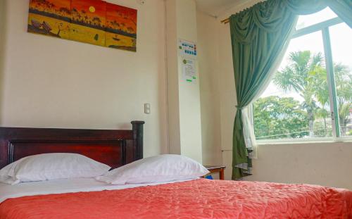 a bedroom with a bed with a red bedspread and a window at Hotel Real Amazónico in Puyo