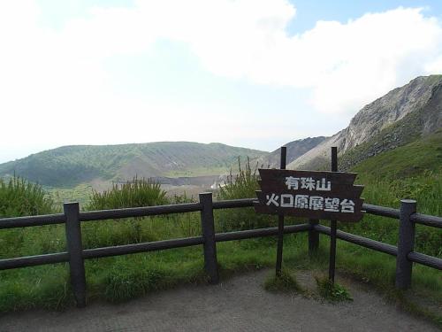 a sign in front of a fence with mountains in the background at Guest house HiDE in Lake Toya