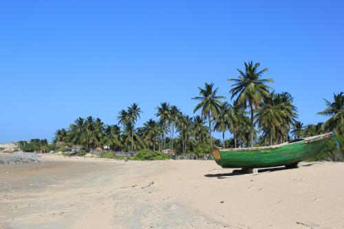 a green boat sitting on a beach with palm trees at Pousada Lacula in Praia de Moitas