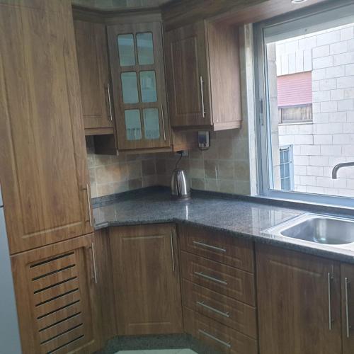 a kitchen with wooden cabinets and a sink and a window at شقة مفروشة في ام اذينة in Amman