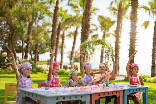 a group of children sitting at a table with their hands in the air at Akka Antedon Hotel - Premium Ultra All Inclusive in Beldibi