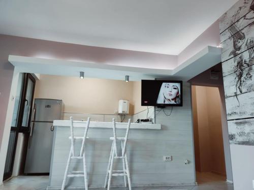 a kitchen with two bar stools and a tv on the wall at Апартамент Съншайн in Burgas