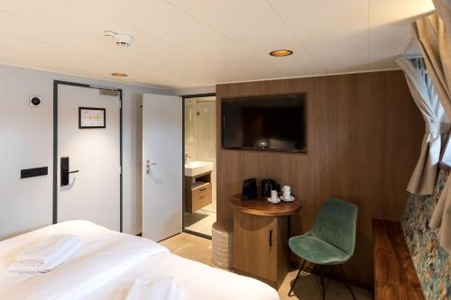 a bedroom with a bed and a chair and a television at Hotelboot Koningin Emma I Kloeg Collection in Vlissingen