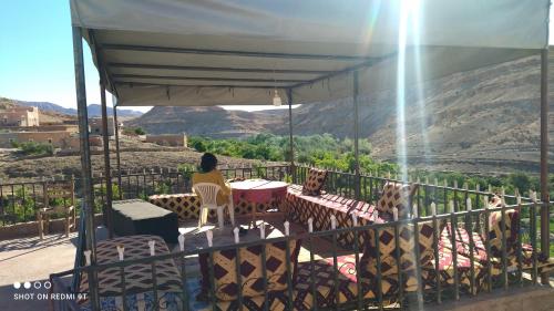 a woman sitting at a table on a balcony with a view at Hôtel familiale les grotte in Aït Ben Haddou