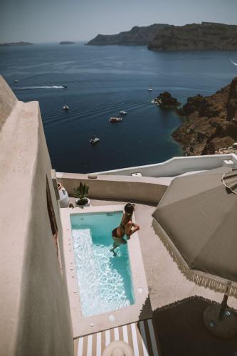 a man sitting in a swimming pool with a view of the ocean at Spitia Santorini Villa Collection in Oia
