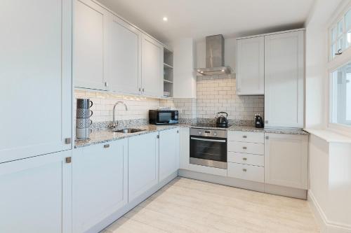a white kitchen with white cabinets and a microwave at Jurassic View Apartment in Lyme Regis