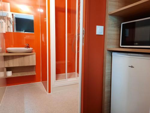 a bathroom with orange walls and a sink and a tv at Kyriad Direct Caen Nord Memorial in Caen