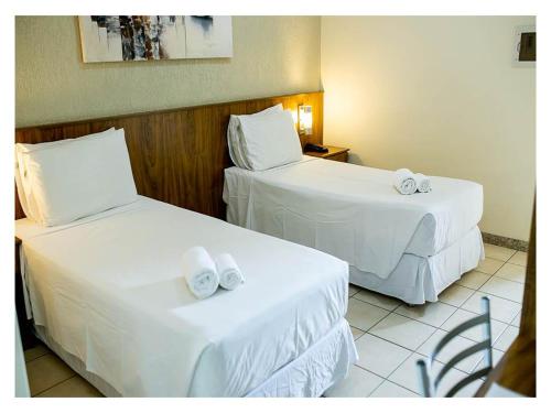 two beds in a hotel room with white sheets at Steel Valley Hotel in Ipatinga