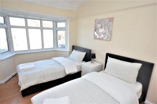 a bedroom with two beds and two windows at London Deluxe 3 Bedroom House with parking space in Dagenham