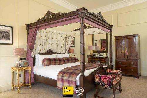 a bedroom with a canopy bed and a chair at The Tudor House Hotel, Tewkesbury, Gloucestershire - The Coaching Inn Group in Tewkesbury