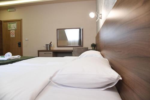 a bedroom with a bed with white pillows and a mirror at Hotel Garden in Novi Sad
