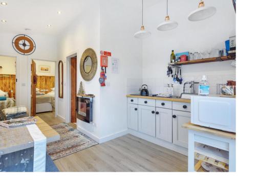 a kitchen with white cabinets and a living room at Minimoore Lodge. Perfect for walkers, cyclists and surfers. in Scorrier