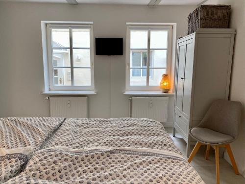 a bedroom with a bed and a chair and two windows at Hafenkoje Husum in Husum
