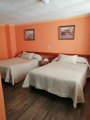 two beds in a room with orange walls at Hotel Las Américas in Morelia
