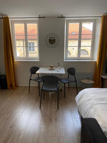 a bedroom with a table and chairs and two windows at Le bastion in Pontarlier