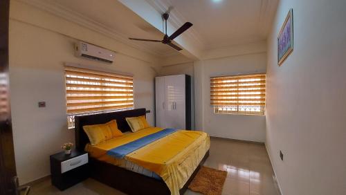 1 Schlafzimmer mit einem Bett mit gelber Bettwäsche und 2 Fenstern in der Unterkunft Luxurious 1 & 2 Bed Apartment at RealShala Homes, Adjiringanor - East Legon in Ashalebotwe