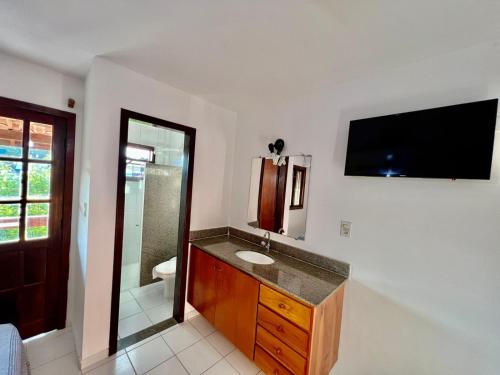 ein Badezimmer mit Waschbecken und einem Fernseher an der Wand in der Unterkunft Duplex Aconchegante Residencial Mont Sinai in Porto Seguro