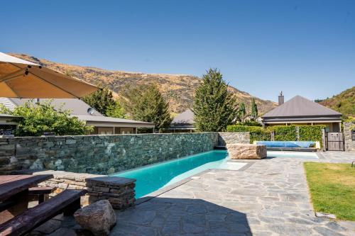 a swimming pool with a stone retaining wall and a bench at Cardrona Cottage - Cardrona Holiday Home in Cardrona