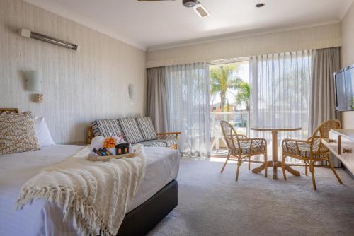 a bedroom with a bed, chair, table and window at South Pacific Palms Motor Inn in Tuncurry