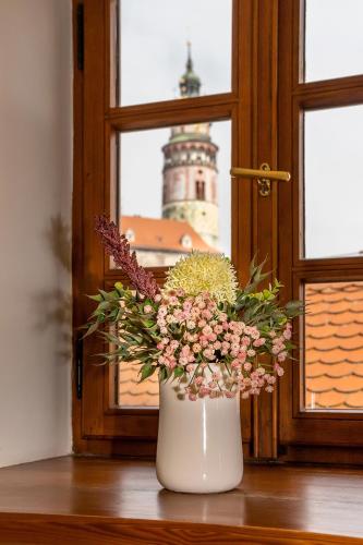 a white vase with flowers in front of a window at Penzion Maštal in Český Krumlov