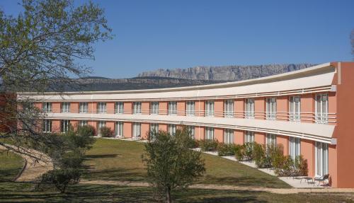 a large building with trees and mountains in the background at Hôtel Mount Venturi - Aix-En-Provence Sainte-Victoire - Bar & Restaurant & Padel in Rousset